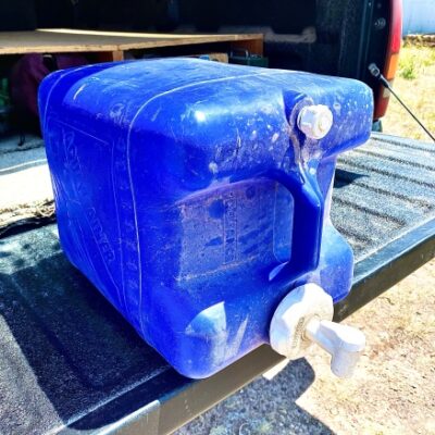 A blue 5-gallon Reliance Aqua-tainer sitting on a truck tailgate.